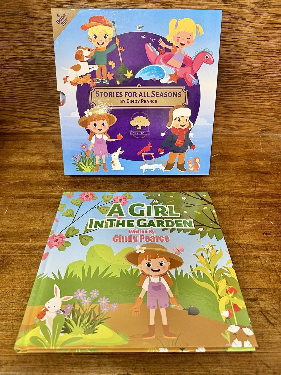 Stories for all Seasons Slipcase and A Girl in the Garden Book on a wooden surface, featuring colorful illustrations of children and animals.